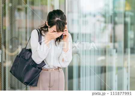 オフィスビルでトラブル・クレーム・悲報の連絡を受けて顔を覆うビジネスウーマン・ワーキングウーマン 111877991