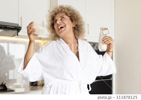 Joyful Woman in White Robe Enjoying Fresh Milk in Kitchen 111878125
