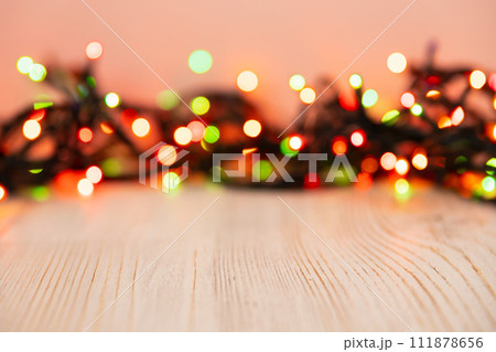 Blurred product background with Christmas New Year colorful light bulbs garland and wooden table. Selective focus, copy space for beauty product packaging, advertising backdrop. Empty place 111878656