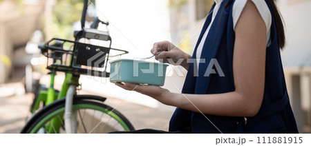 Young businesswoman while eating a lunch box sitting on a staircase during a break from work, concept healthy food using a bicycle for driving, Eco friendly vehicle, sustainable lifestyle concept 111881915