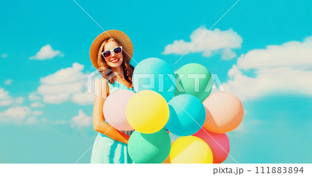Happy smiling young woman with bunch of colorful balloons on the field on a blue sky background Happy smiling young woman with bunch of colorful balloons on the field on a blue sky background 111883894