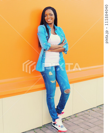 Portrait of happy smiling young african woman in the city on colorful orange background Portrait of happy smiling young african woman in the city on colorful orange background 111884040