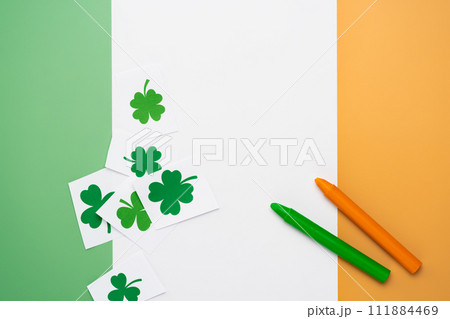 Irish flag made from color paper with cut out shamrock clover and crayons. DIY creative art craft activity for kids on St Patricks hobby 111884469