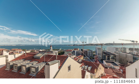 Panorama showing red roofs timelapse and 25 de Abril Bridge, Iconic suspension bridge over Tagus River in Lisbon, Portugal. 111884663