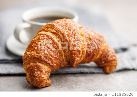 Baked tasty croissant and coffee cup on kitchen table. Baked tasty croissant and coffee cup on kitchen table. 111885620