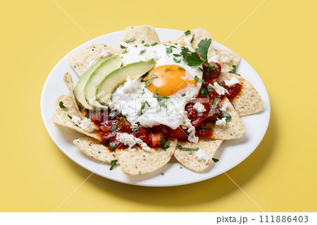 Traditional Mexican breakfast red chilaquiles with egg on yellow background Traditional Mexican breakfast red chilaquiles with egg on yellow background 111886403