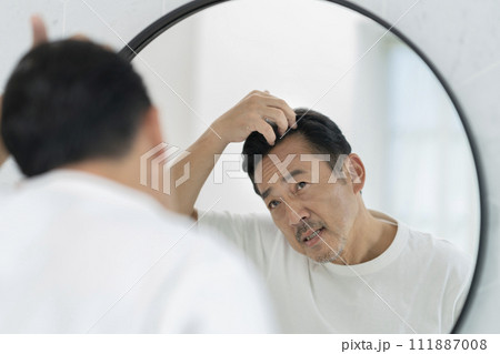 鏡を見ながら髪の生え際を気にする50代の男性 111887008