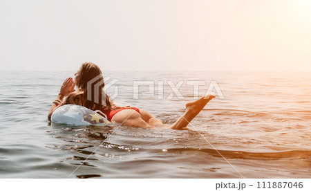 Woman summer sea. Happy woman swimming with inflatable donut on the beach in summer sunny day, surrounded by volcanic mountains. Summer vacation concept. Woman summer sea. Happy woman swimming with inflatable donut on the beach in summer sunny day, surrounded by volcanic mountains. Summer vacation concept. 111887046