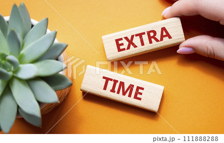 Extra time symbol. Concept word Extra time on wooden blocks. Beautiful orange background with succulent plant. Businessman hand. Business and Extra time concept. Copy space Extra time symbol. Concept word Extra time on wooden blocks. Beautiful orange background with succulent plant. Businessman hand. Business and Extra time concept. Copy space 111888288