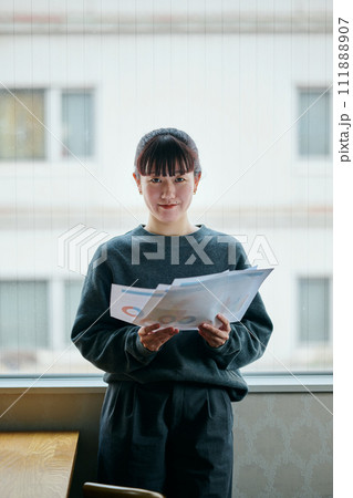 窓際で資料を持って立つ若い女性 111888907