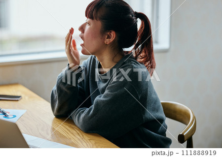 デスクであくびをして眠そうな表情の若い女性 111888919