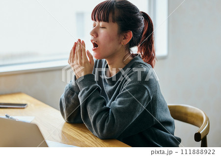 デスクであくびをして眠そうな表情の若い女性 111888922