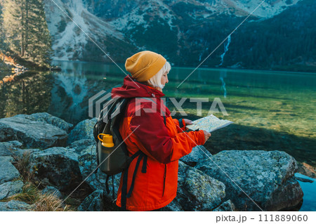 Shot of a senior 60s lost woman with smart phone holding a map while taking in the view from the top of a mountain. Female tourist in mountain read the map. Poland, Tatry Shot of a senior 60s lost woman with smart phone holding a map while taking in the view from the top of a mountain. Female tourist in mountain read the map. Poland, Tatry 111889060