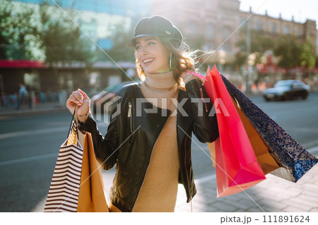 Smiling woman with shopping bags using her phone. Young woman after shopping on the city street. Smiling woman with shopping bags using her phone. Young woman after shopping on the city street. 111891624