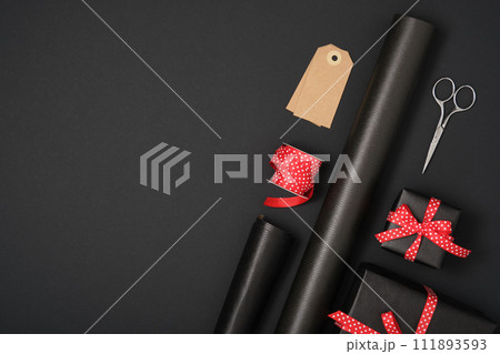 Love gift wrapping. Craft black wrapping paper, red dotted ribbon, gift tag, box, scissors. Copyspace Love gift wrapping. Craft black wrapping paper, red dotted ribbon, gift tag, box, scissors. Copyspace 111893593