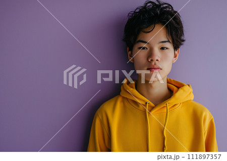Asian serious teenage boy wearing yellow hoodie on purple background 111897357