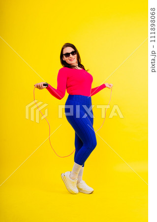 Pretty smiling plump female in sporty top and leggings holding jumping rope in hands 111898068