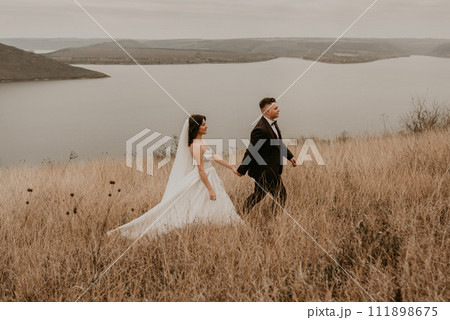 couple wedding newlyweds in walk hug kissing on tall grass on mountain above the river 111898675