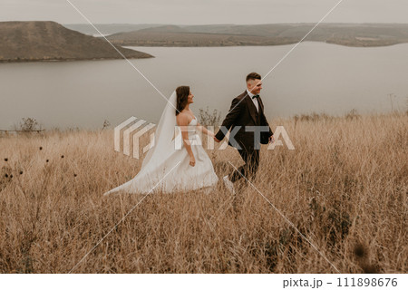 couple wedding newlyweds in walk hug kissing on tall grass on mountain above the river couple wedding newlyweds in walk hug kissing on tall grass on mountain above the river 111898676