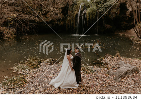 bride hugs groom near small pond lake river waterfall Burbun 111898684