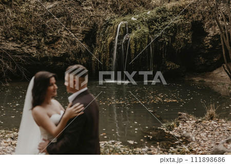 bride in white wedding dress and long veil hugs groom in a suit small pond lake river waterfall Burbun bride in white wedding dress and long veil hugs groom in a suit small pond lake river waterfall Burbun 111898686