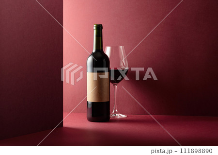 Bottle and glass of red wine on a red background. 111898890