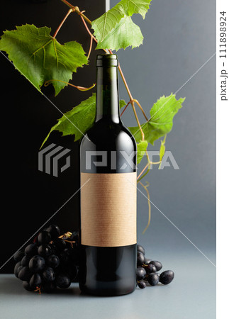 Bottle of red wine with blue grapes and vine branches. 111898924