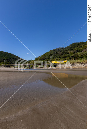 干潮での砂模様と青空、潮止まりに反射するJR九州日南線黄色いDLキハ40 111903049