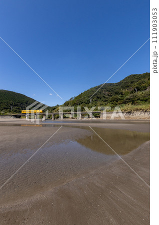 干潮での砂模様と青空、潮止まりに反射するJR九州日南線黄色いDLキハ40 111903053