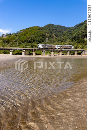 干潮での砂模様と青空、潮止まりに反射するJR九州日南線観光列車海幸山幸 111903058