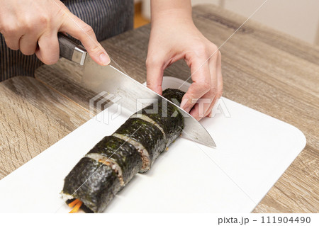 巻き寿司を切り分ける女性の手元 111904490