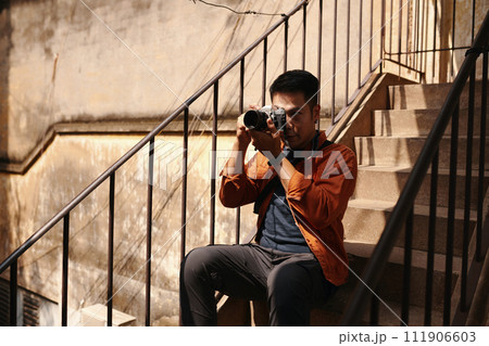 Photographer sitting on steps and taking photos in old decaying building 111906603