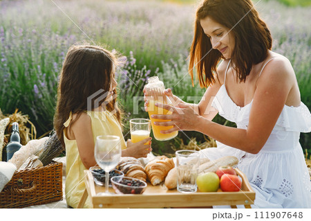Mother with little daughter on lavender background. Beautiful woman and cute baby playing in meadow field. Family in a picnic. Mother with little daughter on lavender background. Beautiful woman and cute baby playing in meadow field. Family in a picnic. 111907648