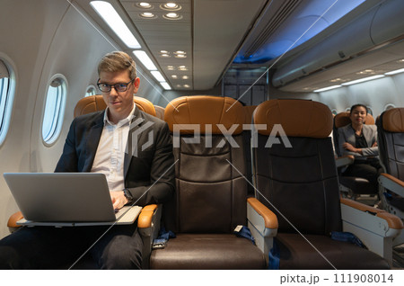 Businessman using laptop while sitting in airplane cabin. Business work and travel concept. 111908014