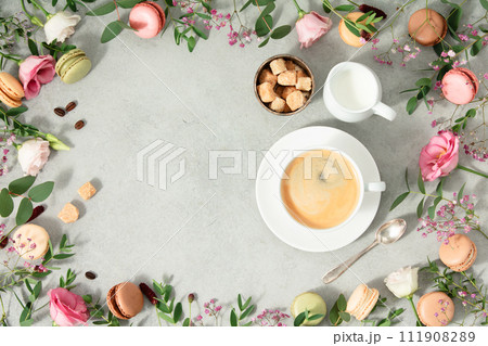White cup of coffee and Frame made of Spring flowers and different types of macaroons White cup of coffee and Frame made of Spring flowers and different types of macaroons 111908289