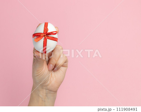 Easter egg with a red ribbon in a female hand. 111908491