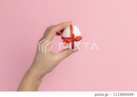 Easter egg with a red ribbon in a female hand. 111908499