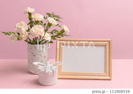 Bouquet of carnations in a vase with a gift box and a photo frame. Bouquet of carnations in a vase with a gift box and a photo frame. 111908539