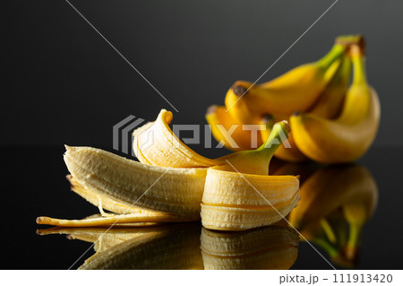 Ripe juicy bananas on a black reflective background. 111913420
