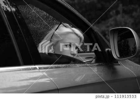A relaxing moment when a beautiful woman sits in the front seat of a car and looks out the open door. Black and white image. AI-generated item. A relaxing moment when a beautiful woman sits in the front seat of a car and looks out the open door. Black and white image. AI-generated item. 111913533