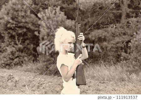 A young beautiful blonde girl shoots from a rifle. AI-generated item. 111913537