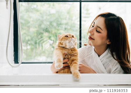 Bath time bonding, a woman holds her Scottish Fold cat in the bathtub, radiating happiness and the warmth of pet companionship in the bathroom. Bath time bonding, a woman holds her Scottish Fold cat in the bathtub, radiating happiness and the warmth of pet companionship in the bathroom. 111916353