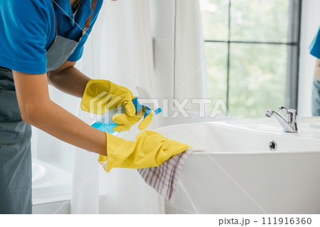 Focused on chores a woman in uniform sprays and cleans bathroom sink and faucet. Her dedication to housework emphasizes purity hygiene and shining fixtures at home. spray cleaner Focused on chores a woman in uniform sprays and cleans bathroom sink and faucet. Her dedication to housework emphasizes purity hygiene and shining fixtures at home. spray cleaner 111916360