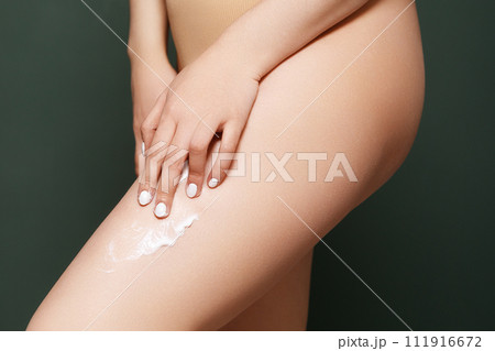 Woman applying body cream on her leg in bedroom 111916672