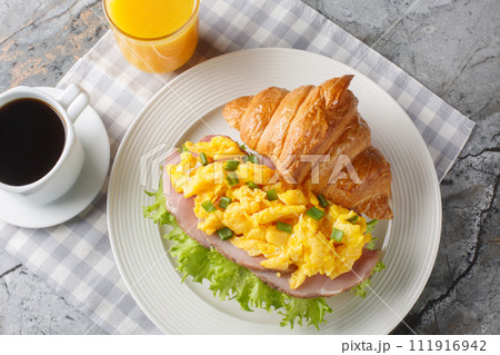 Breakfast Croissant Sandwich with Scrambled Eggs and Ham Served with Orange Juice and Coffee Close-up. Horizontal top view Breakfast Croissant Sandwich with Scrambled Eggs and Ham Served with Orange Juice and Coffee Close-up. Horizontal top view 111916942