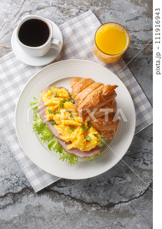 Scrambled eggs ham croissant served with orange juice and coffee close-up. Vertical top view Scrambled eggs ham croissant served with orange juice and coffee close-up. Vertical top view 111916943