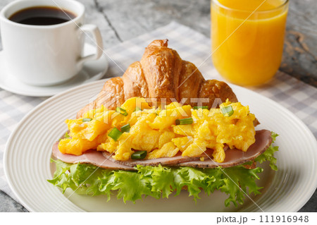 Breakfast Croissant Sandwich with Scrambled Eggs and Ham Served with Orange Juice and Coffee Close-up. Horizontal 111916948