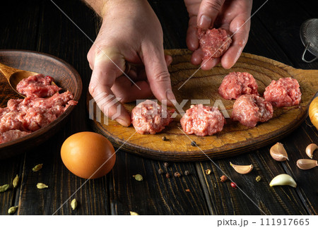 The chef hand places a meatball on the kitchen board. Preparing meat on the kitchen table for lunch. Cooking recipes and nutrition concept The chef hand places a meatball on the kitchen board. Preparing meat on the kitchen table for lunch. Cooking recipes and nutrition concept 111917665
