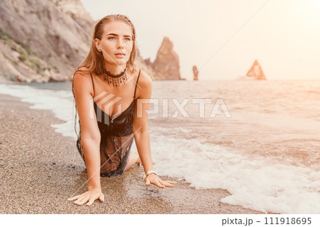 Woman summer travel sea. Happy tourist in black dress enjoy taking picture outdoors for memories. Woman traveler posing on sea beach surrounded by volcanic mountains, sharing travel adventure journey Woman summer travel sea. Happy tourist in black dress enjoy taking picture outdoors for memories. Woman traveler posing on sea beach surrounded by volcanic mountains, sharing travel adventure journey 111918695