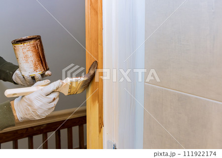 Wooden door frames moldings are painted with stain by worker using brush 111922174